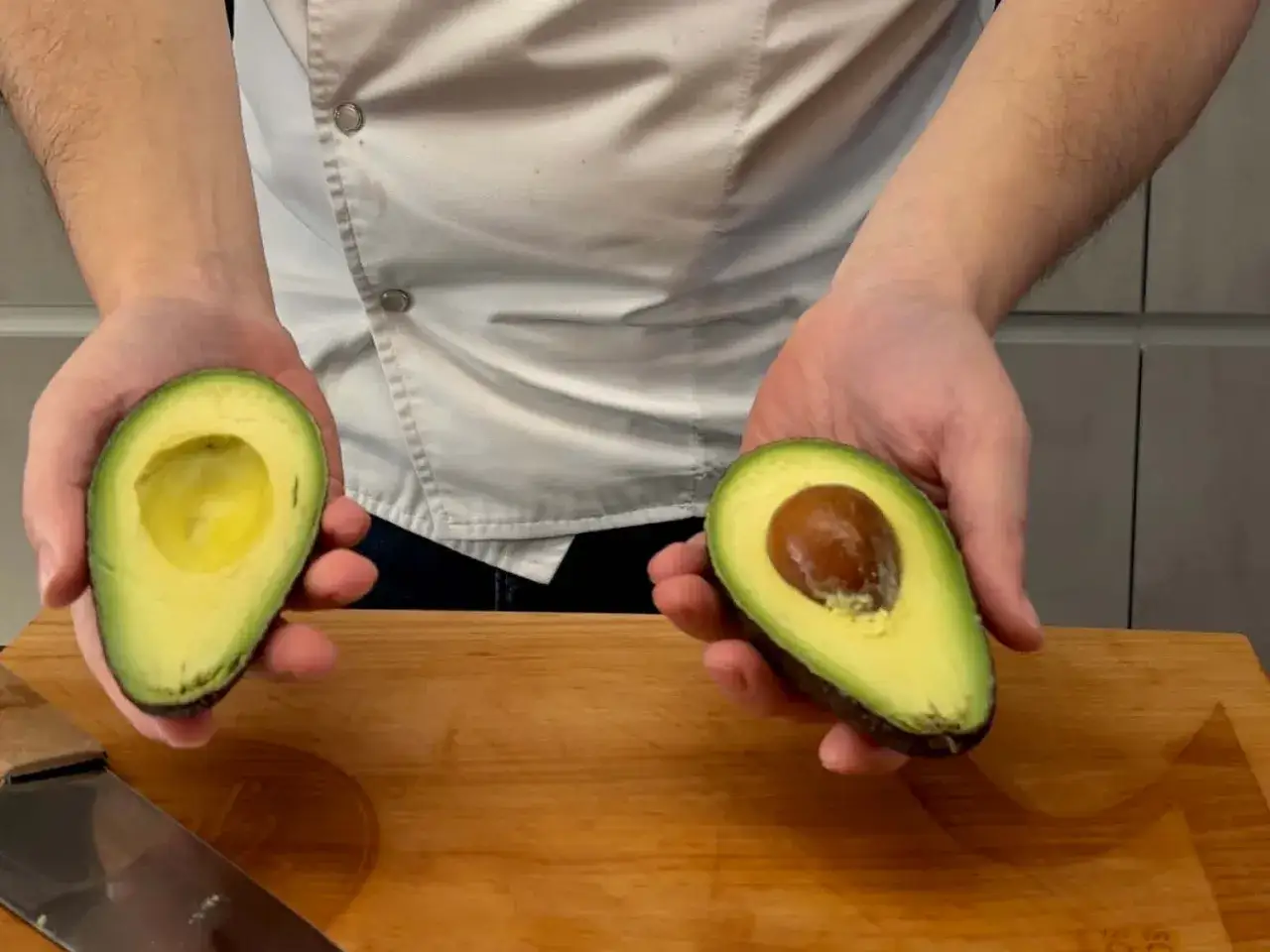 Hände halten zwei Avocadehälften. Eine ist kernlos, die andere mit Kern. So lässt man die Avocado reifen.