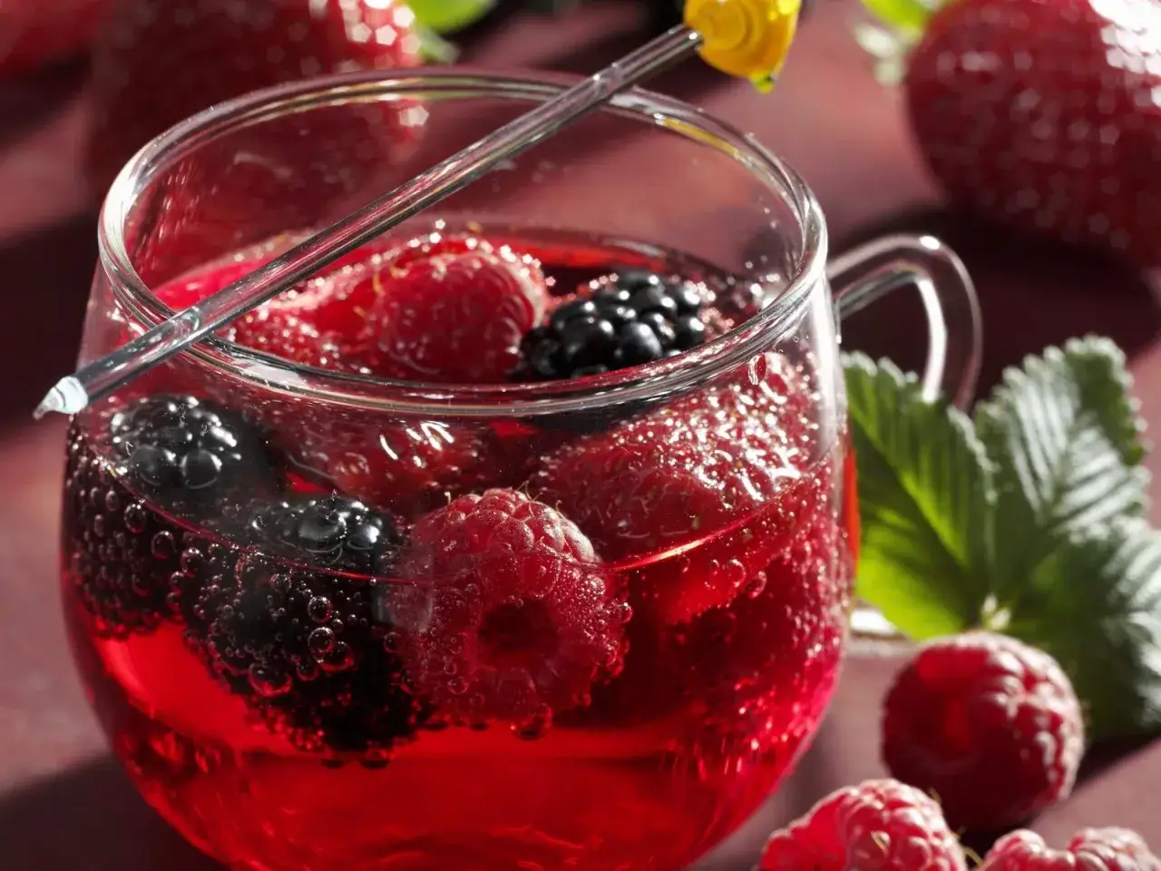 Erfrischende alkoholfreie Bowle mit Himbeeren, Brombeeren und Erdbeeren in einem Glas, garniert mit einem gelben Dekorationselement.