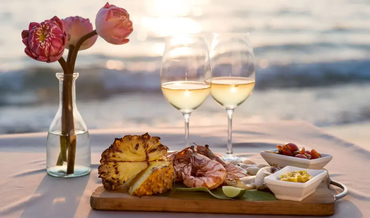Romantisches Abendessen am Strand: Gegrillte Meeresfrüchte, Ananas und zwei Gläser Weißwein – die perfekte Antwort auf die Frage, welcher Wein zu Fisch passt.