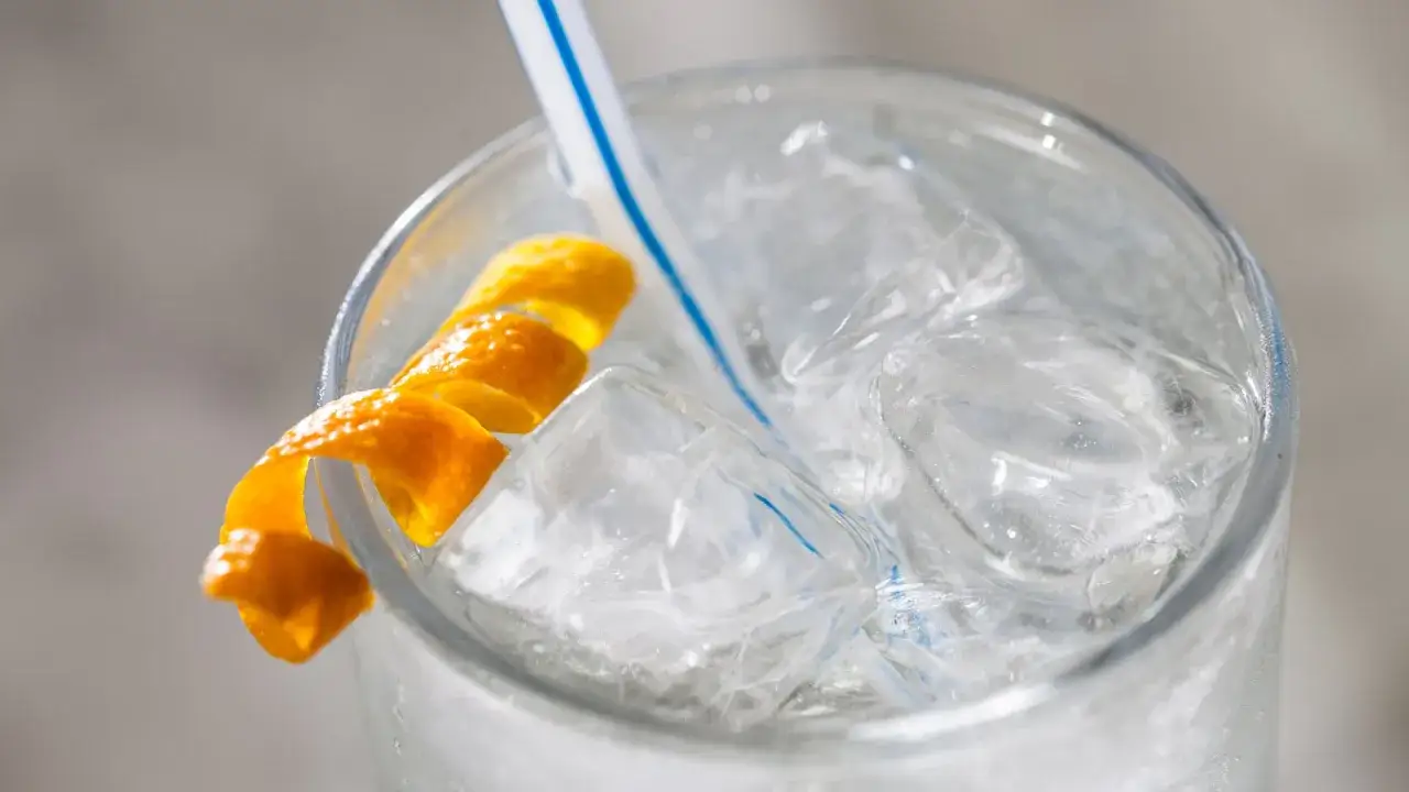 Erfrischender Gin Bitter mit Eiswürfeln, einem blauen Strohhalm und einer Orangenzeste.