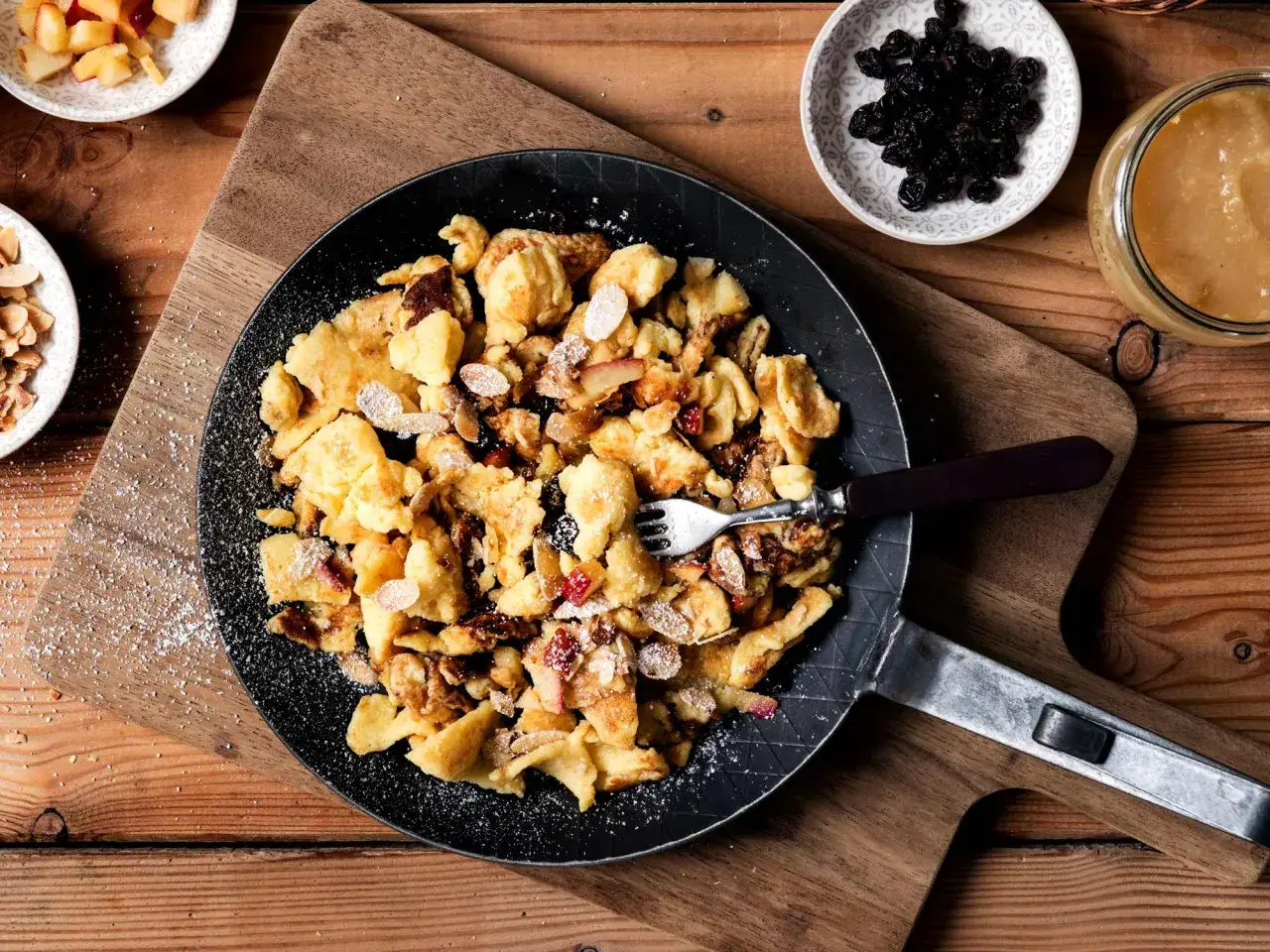 Kaiserschmarrn rezept: Ein goldbrauner Kaiserschmarrn mit Rosinen, Mandeln und Apfelst&uuml;cken in einer Pfanne, best&auml;ubt mit Puderzucker.