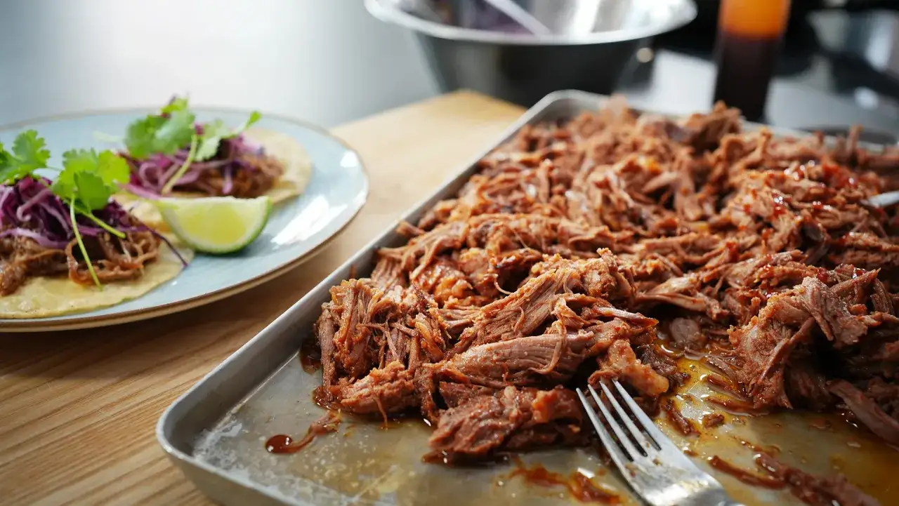 Saftiges pulled pork in einer Schale, daneben zwei Tacos mit Rotkohl und Koriander.