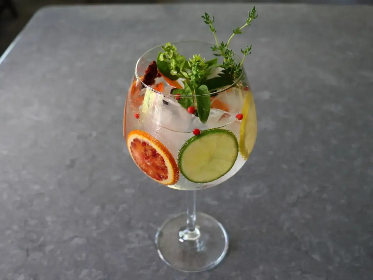 Klassischer Gin Tonic: Eis, Limette, Blutorange, Zitrone, Kräuter und rosa Pfefferbeeren für das perfekte Rezept.