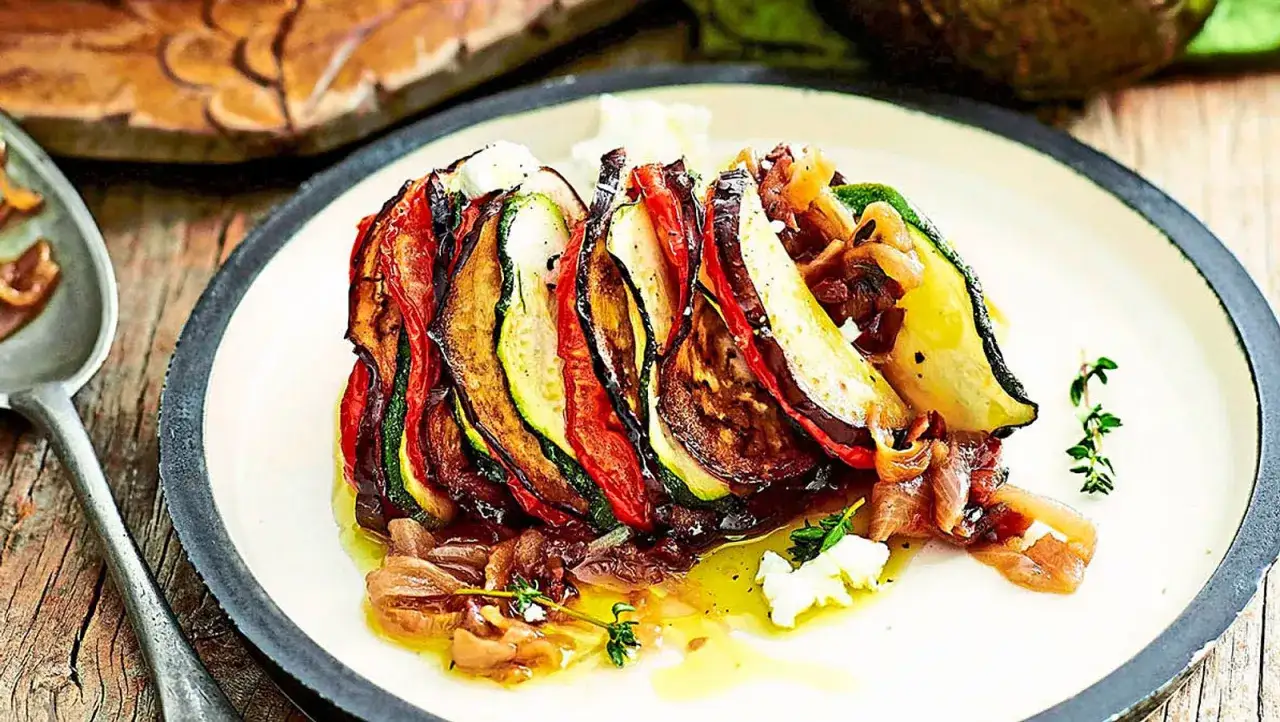 Ein kunstvoll geschichtetes Ratatouille-Rezept mit Zucchini, Aubergine und Tomaten, garniert mit Kr&auml;utern und K&auml;se.