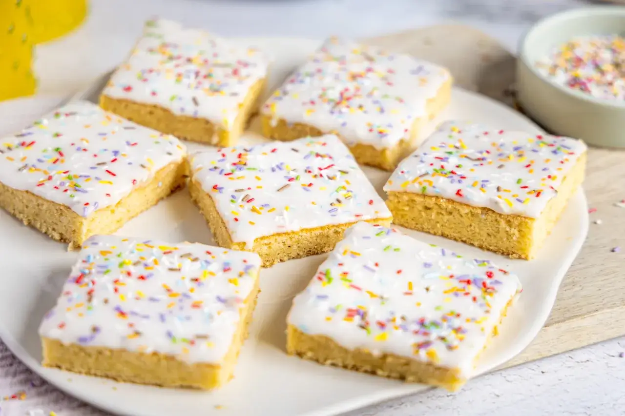 Sieben quadratische Stücke Fantakuchen mit weißer Glasur und bunten Streuseln, ein einfaches Fantakuchen Tassenrezept.