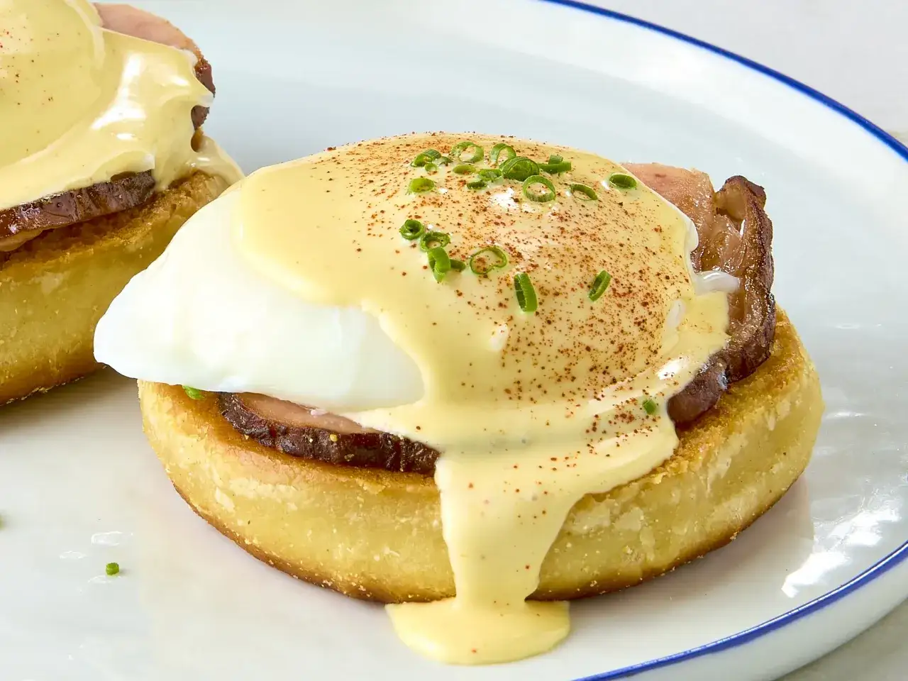 Ein perfekt zubereitetes Egg Benedict mit pochiertem Ei, Schinken und cremiger Sauce Hollandaise, bestreut mit Schnittlauch und Paprikapulver.
