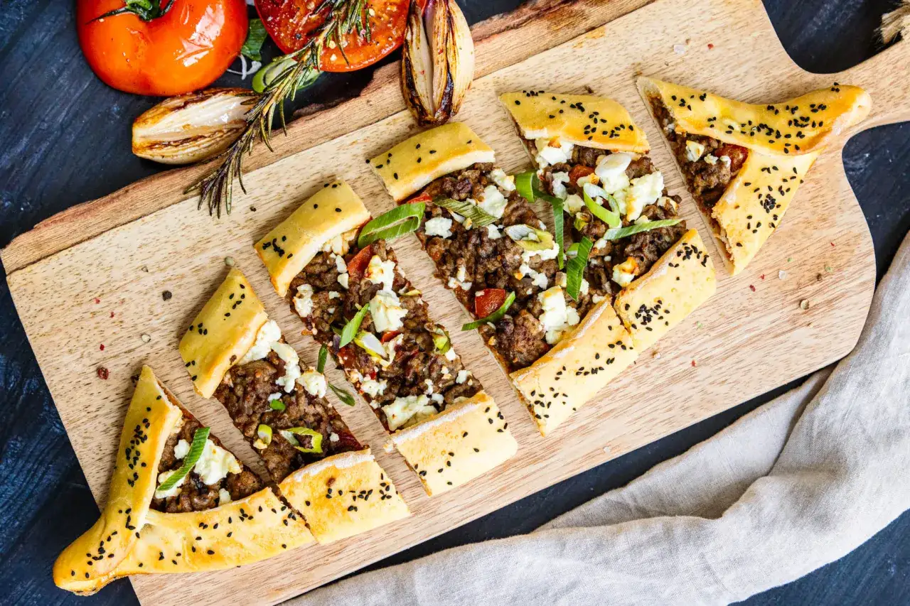 Ein leckeres Pide Rezept: Fladenbrot mit Hackfleisch, Feta und Frühlingszwiebeln, serviert mit gerösteten Tomaten und Zwiebeln.