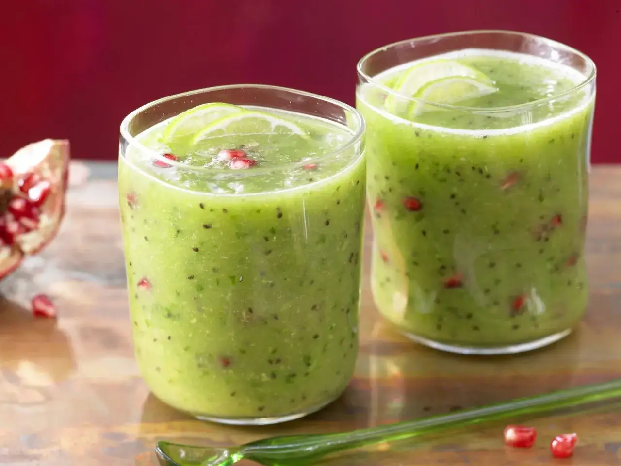 Erfrischender Kiwi-Cocktail mit Granatapfelkernen und Limettenscheiben, garniert mit einer grünen Löffel.