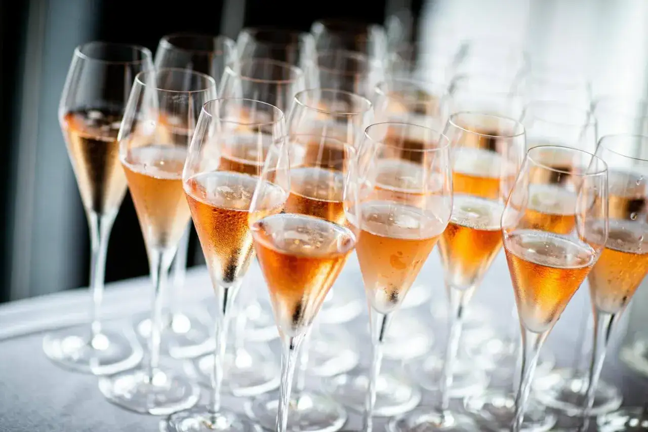 Reihe von Champagnergläsern mit Rosé-Champagner, bereit für den Genuss. So trinkt man Champagner: mit Stil und Freude.