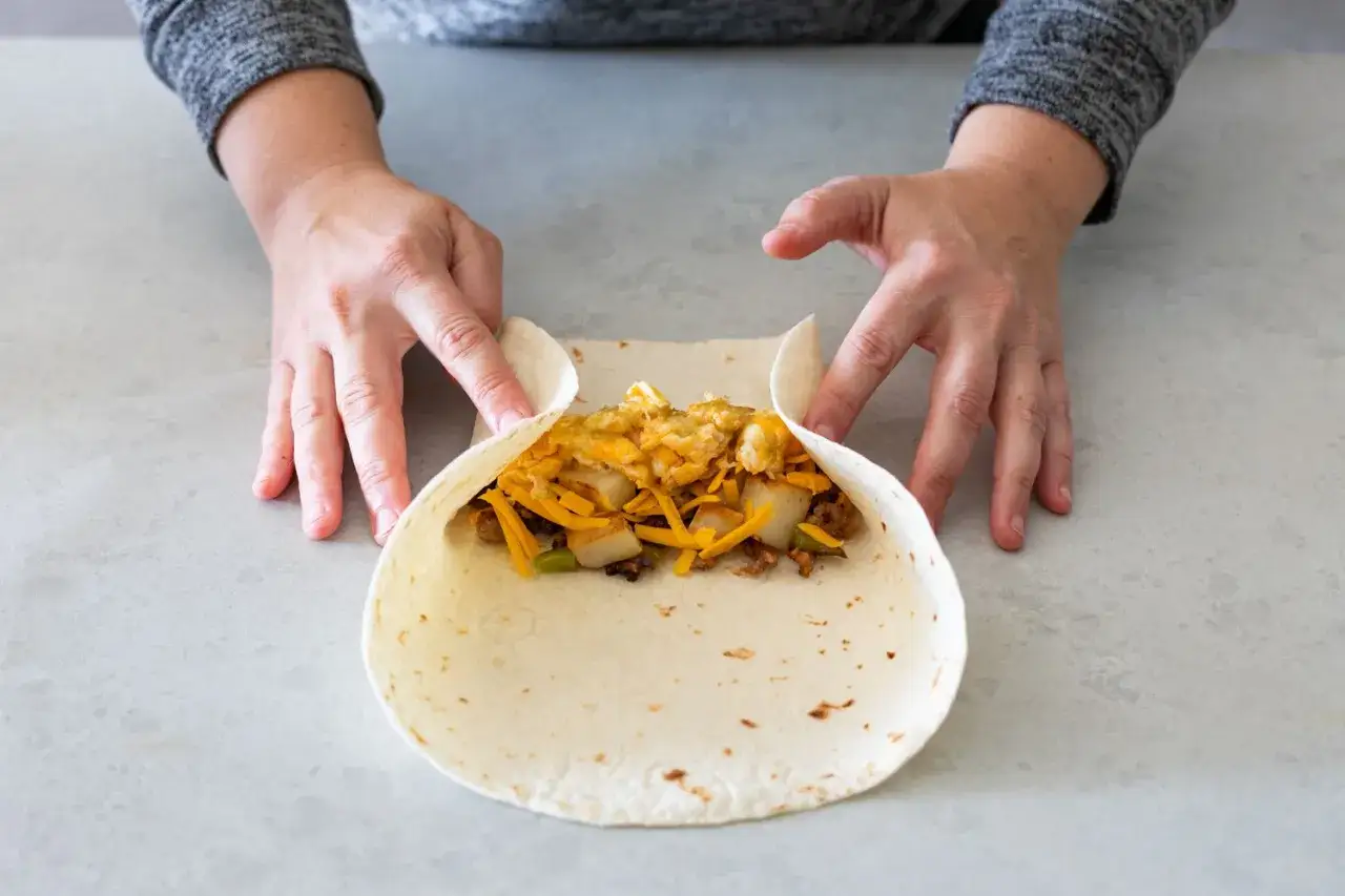 Hände falten wraps mit herzhafter Füllung aus Kartoffeln, Käse und Rührei.