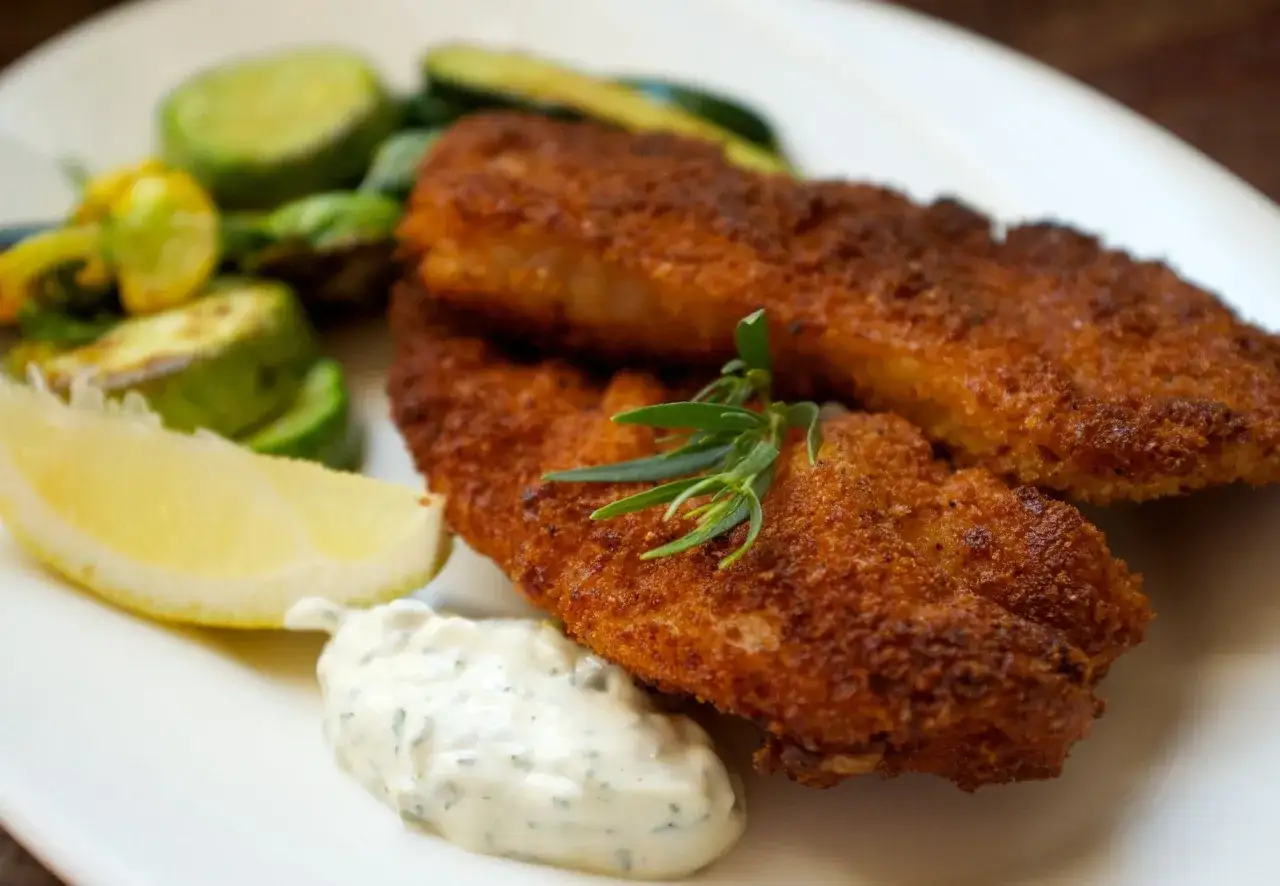 Zwei knusprig panierte Filets von red snapper mit Zitronenspalte, Dip und gegrilltem Gemüse.
