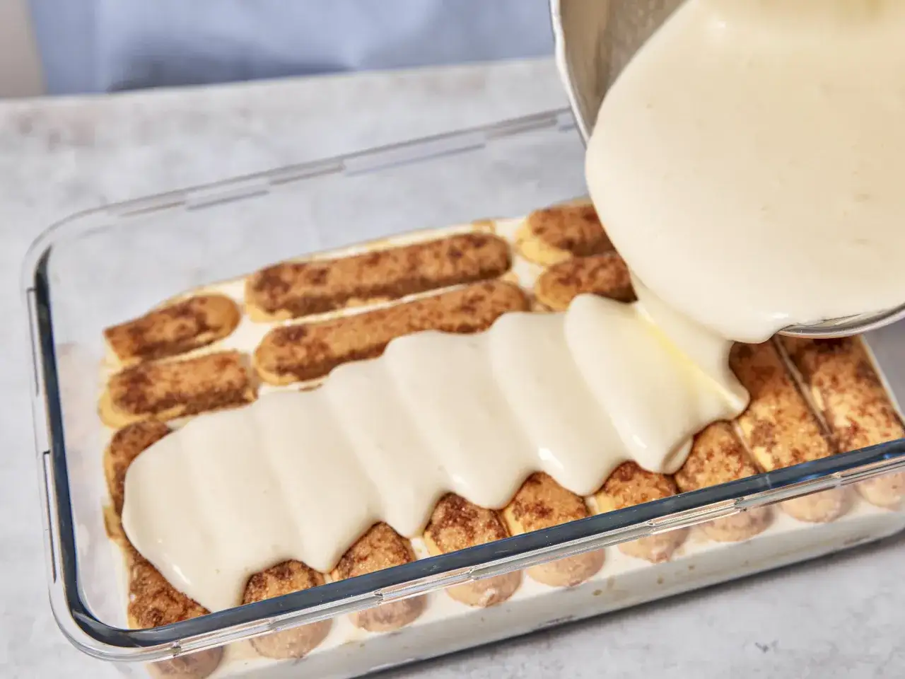 Cremige Tiramisu-Schicht wird über Löffelbiskuits gegossen. Ein Schritt im perfekten Tiramisu Rezept.
