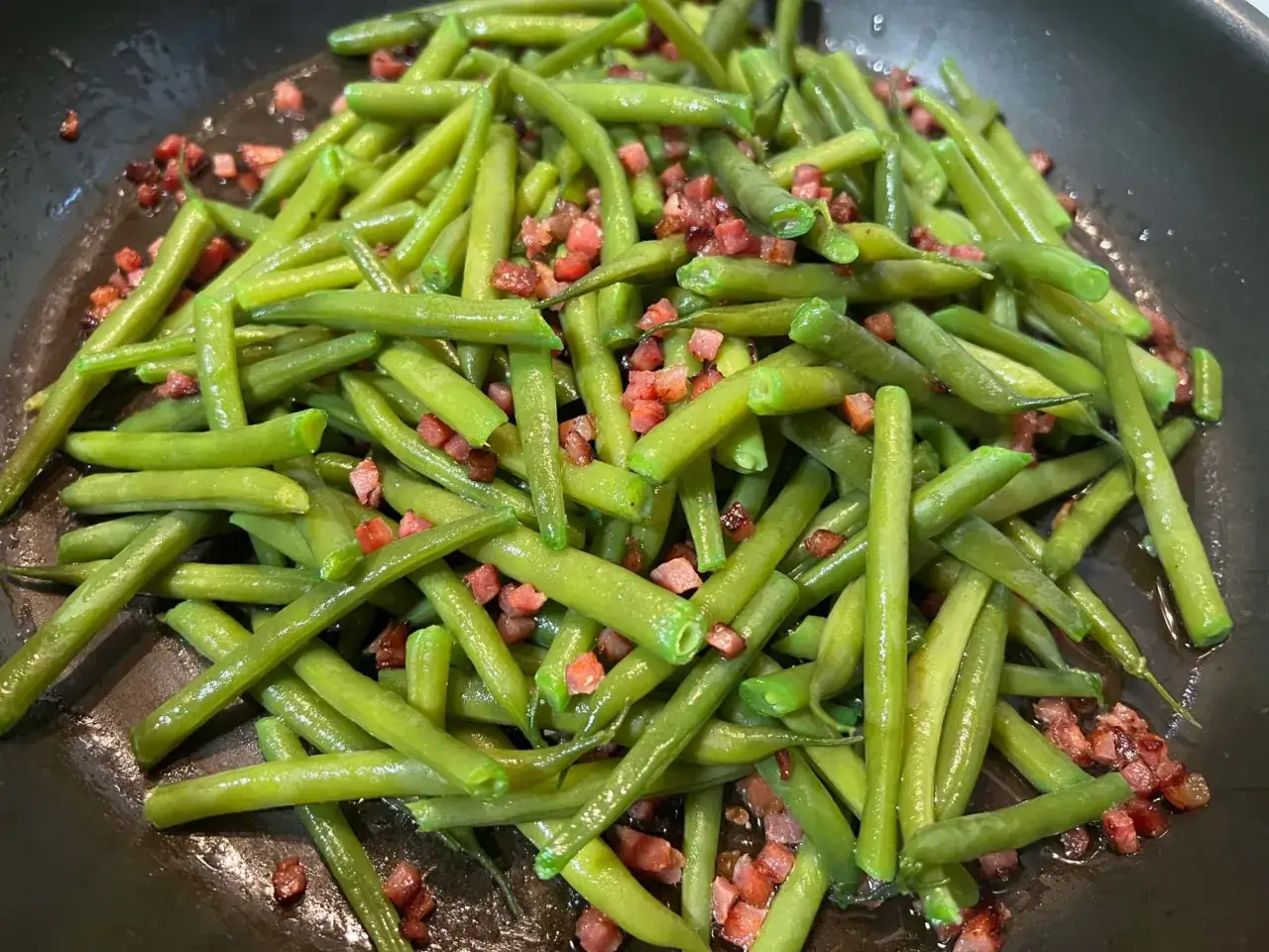 Grüne Bohnen mit Speck, ein einfaches und leckeres speckbohnen rezept, werden in einer Pfanne zubereitet.