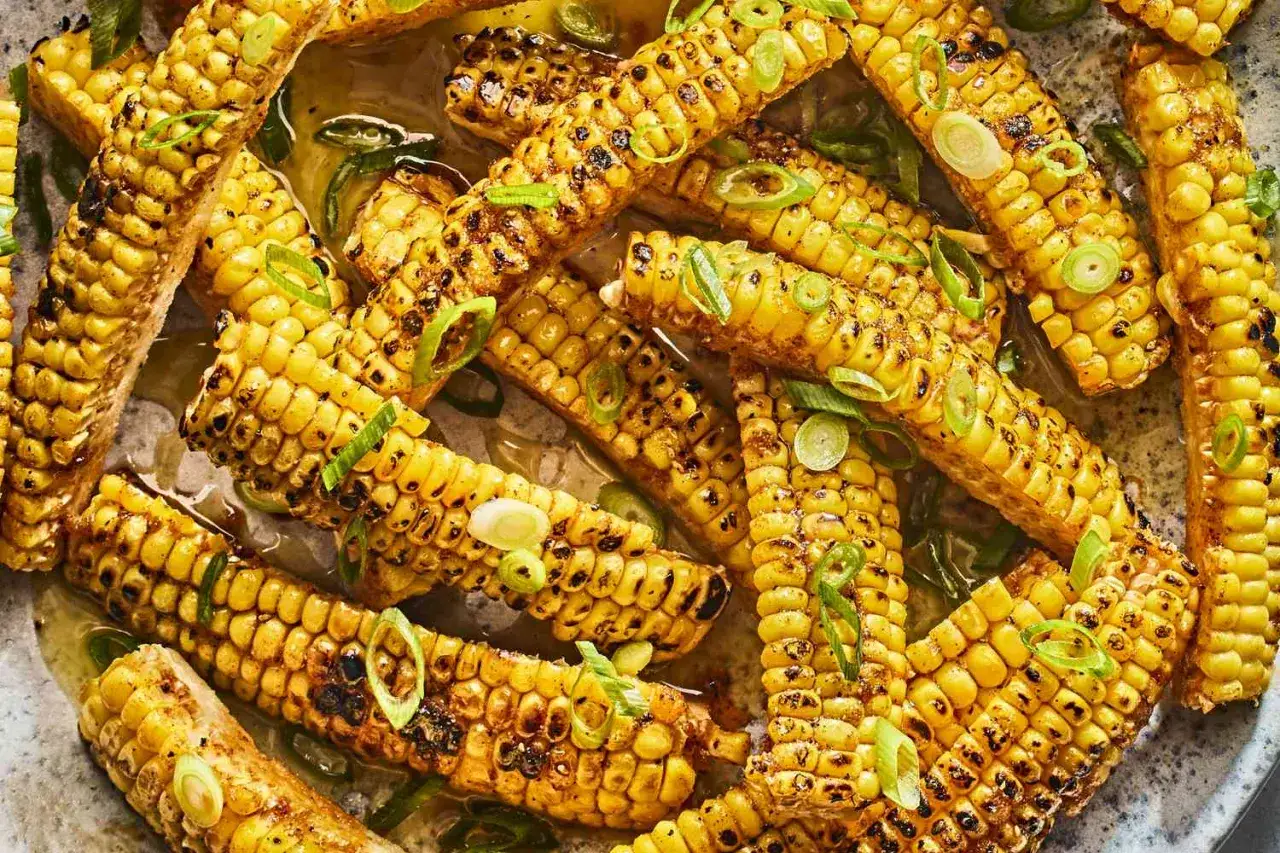 Zuckermais grillen: goldgelbe Kolben mit leichten Röstspuren, garniert mit frischen Frühlingszwiebelringen in einer köstlichen Sauce.