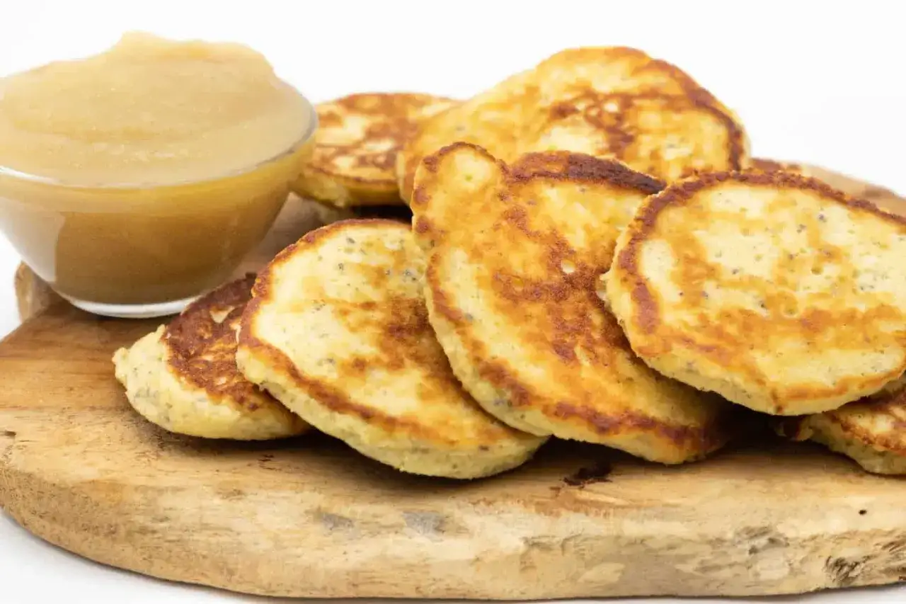 Goldbraune Quarkkeulchen ohne Kartoffeln, serviert mit Apfelmus auf einem Holzbrett. Ein Genuss für jeden Tag!