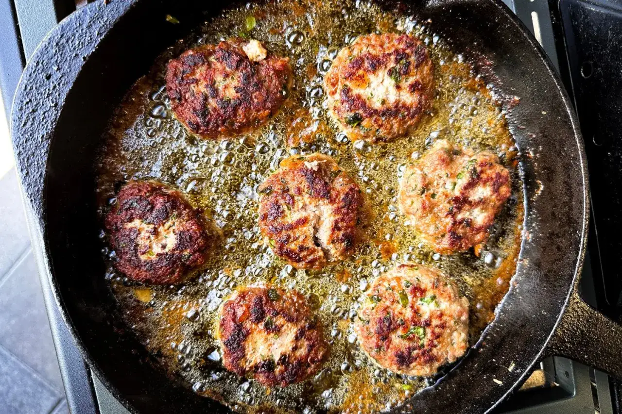 Sechs goldbraune Buletten brutzeln in heißem Öl in einer Gusseisenpfanne. Ein köstliches Buletten Rezept in Aktion.