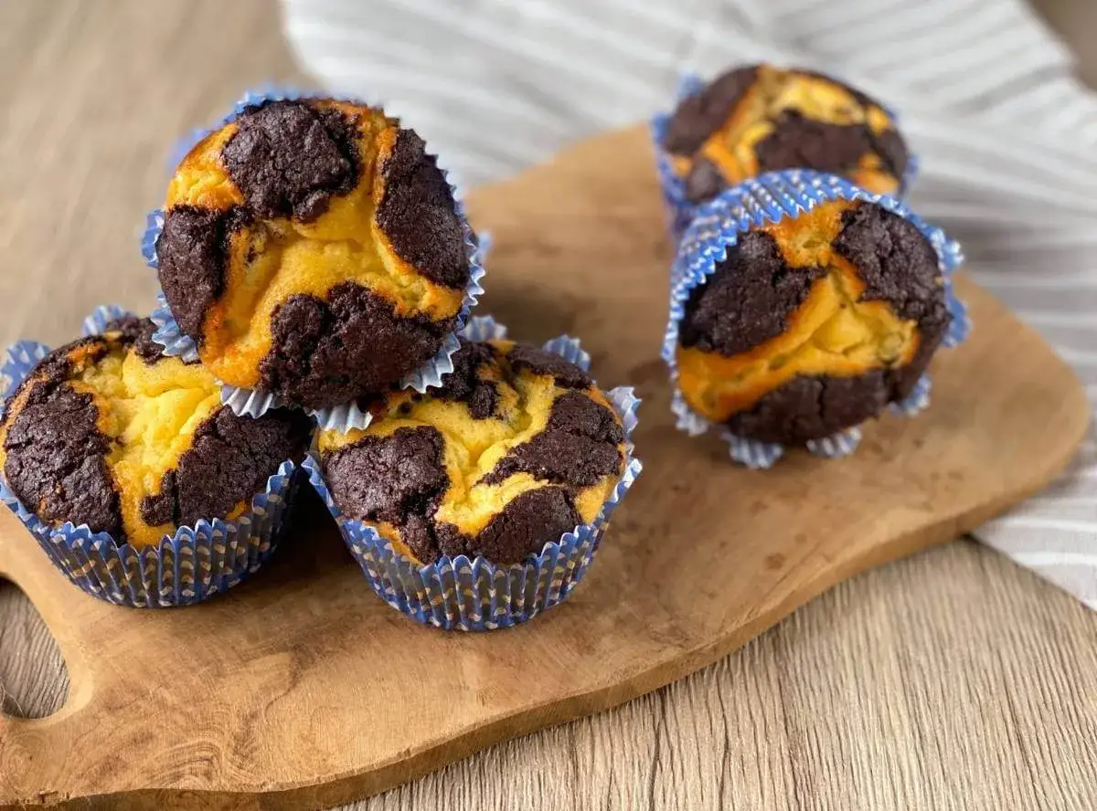 Schokoladen-Vanille-Zupfkuchen-Muffins in blauen Papierförmchen auf einem Holzbrett.
