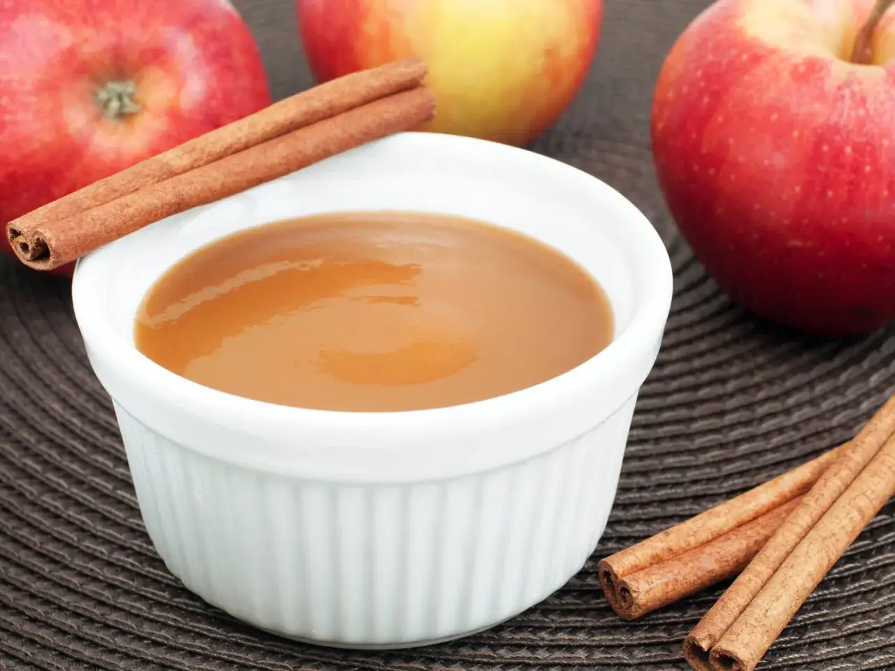 Schüssel mit selbstgemachtem Apfelmus, garniert mit Zimtstangen, daneben frische Äpfel.