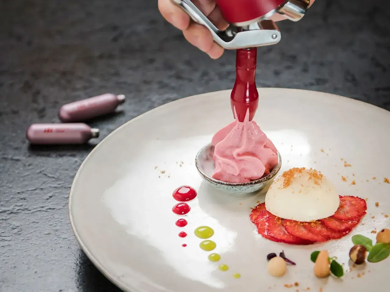 Mit einem Sahnespender wird rosa Espuma herstellen für ein Dessert mit Erdbeeren und weißer Kugel.