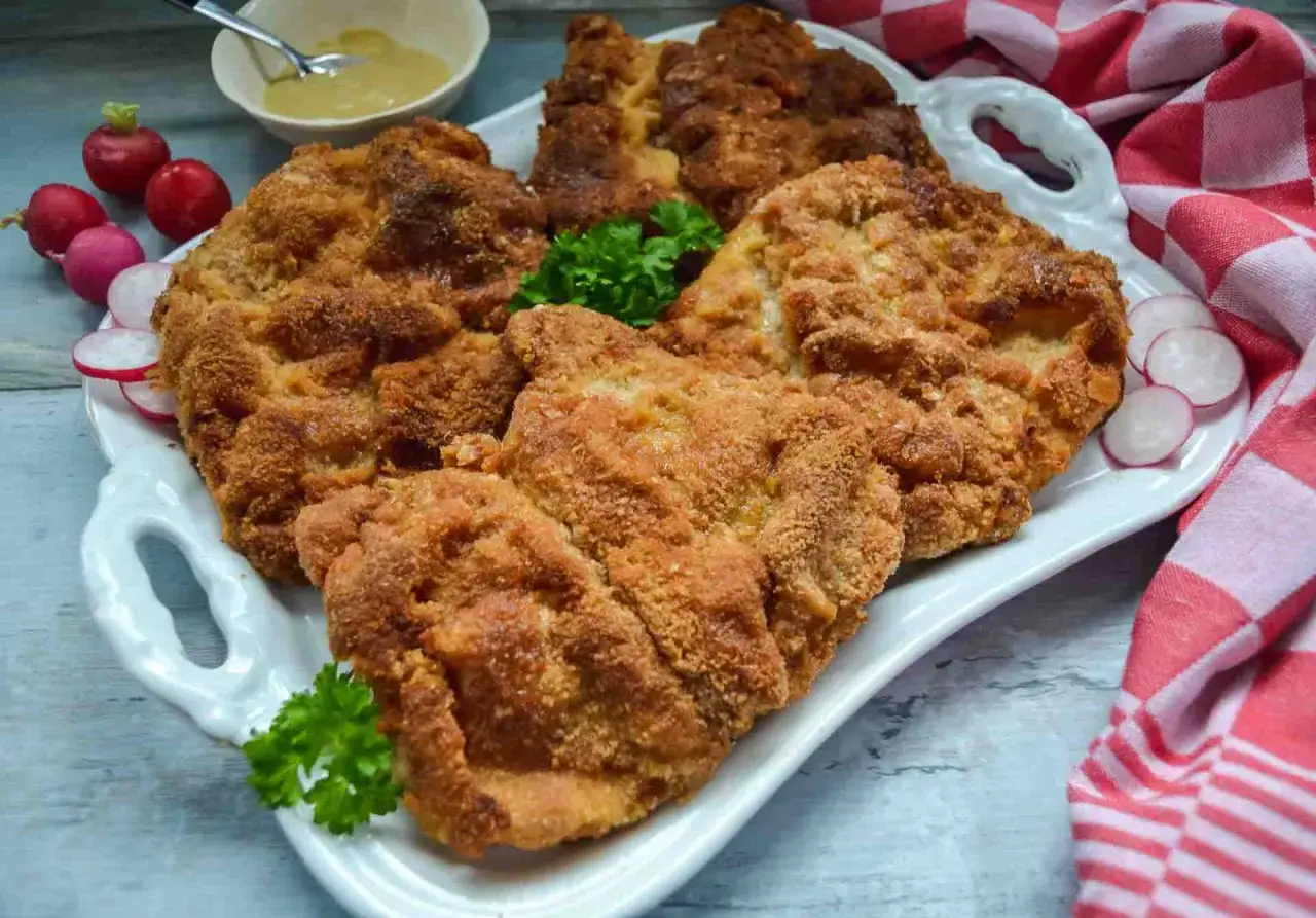 Goldbraune Schnitzel auf weißer Platte, perfekt paniert. Die richtige Schnitzel panieren Reihenfolge macht den Unterschied für diese knusprige Köstlichkeit. Beilage: Radieschen und Senf.