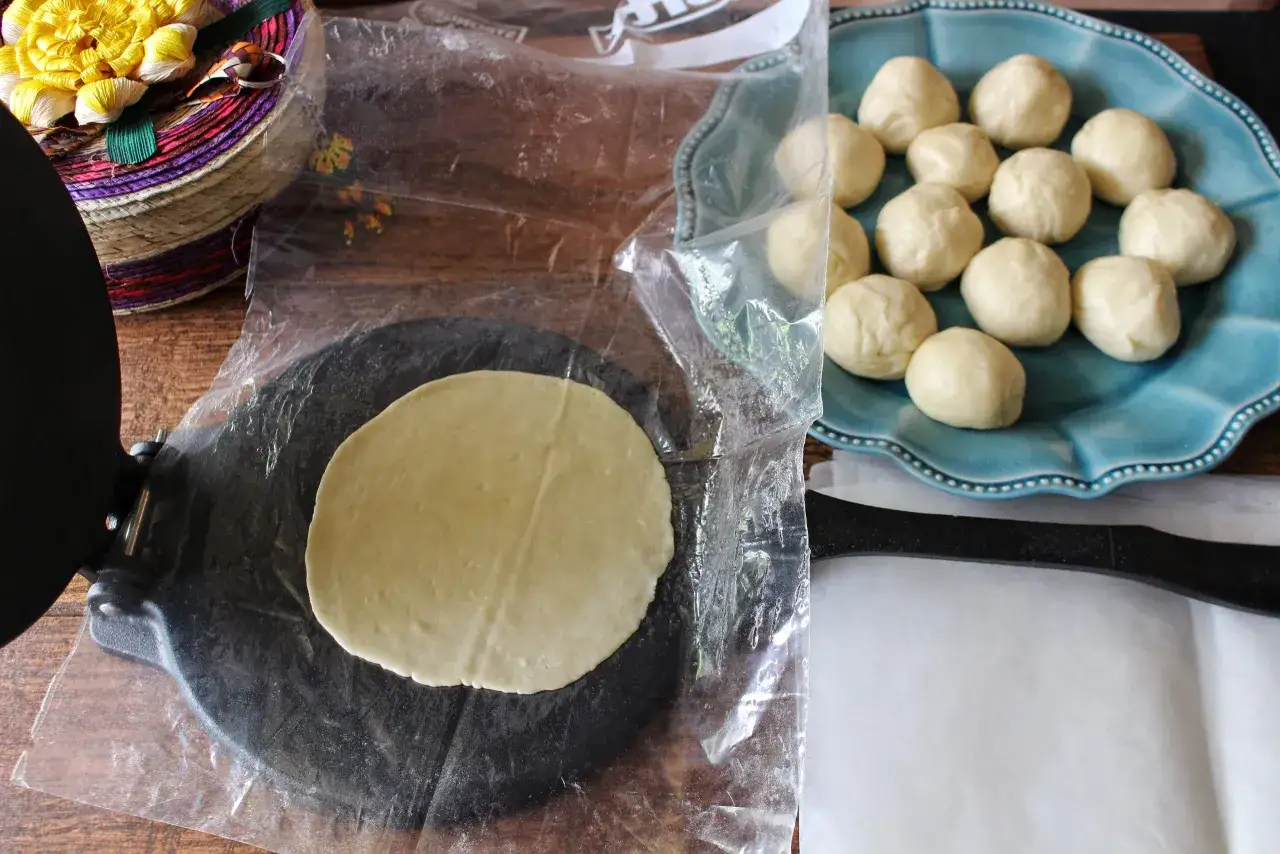 Teigb&auml;llchen liegen bereit f&uuml;r die Zubereitung von wraps selber machen. Ein flacher Teigfladen liegt auf einer Presse.