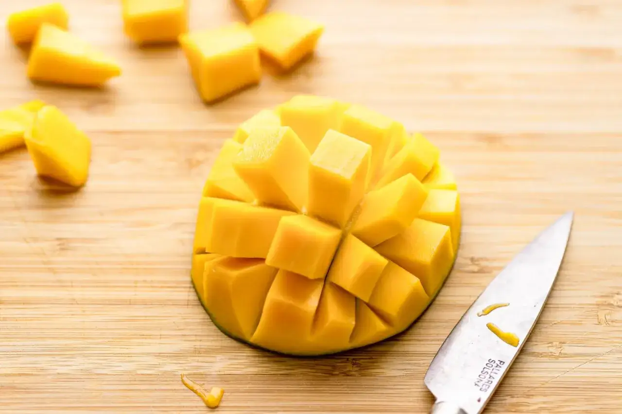 Saftiges Mango schneiden: Ein Messer liegt neben einer aufgeschnittenen Mango, deren Fruchtfleisch würfelig vorbereitet ist.