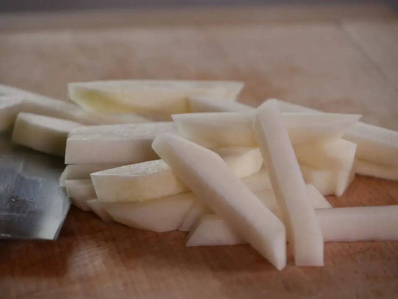 Kohlrabi in Stifte geschnitten, bereit zum Kohlrabi kochen. Ein Messer liegt daneben auf dem Holzbrett.