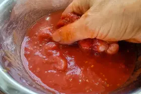 Hand zerdrückt Tomaten in einer Schüssel. So einfach lässt sich Tomatensauce selber machen.