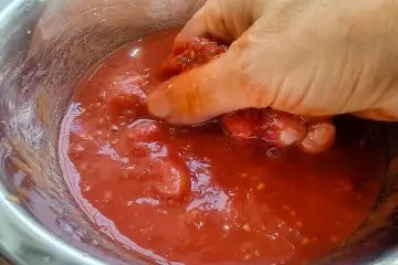 Hand zerdrückt Tomaten in einer Schüssel. So einfach lässt sich Tomatensauce selber machen.