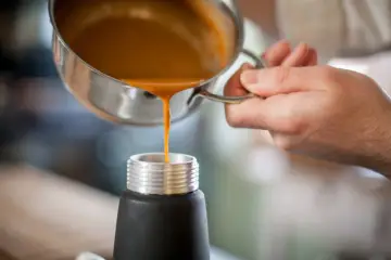 Eine orangefarbene Flüssigkeit wird aus einem Topf in ein schwarzes Gefäß gegossen. Ist das eine Espuma?