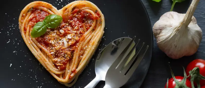 Herzförmige Spaghetti mit Tomatensoße und Basilikum, ein liebevolles Gericht für Pasta Rezepte. Daneben liegen Knoblauch und Tomaten.